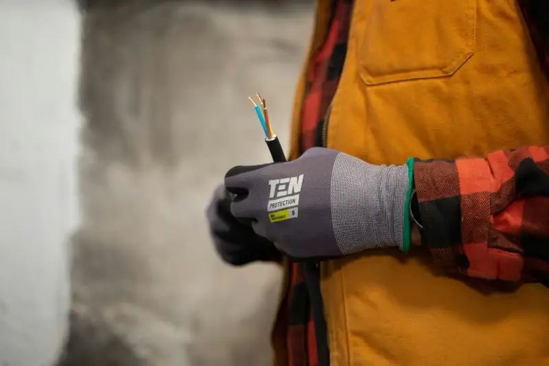 Manos con guantes sujetando un cable eléctrico con los conductores pelados
