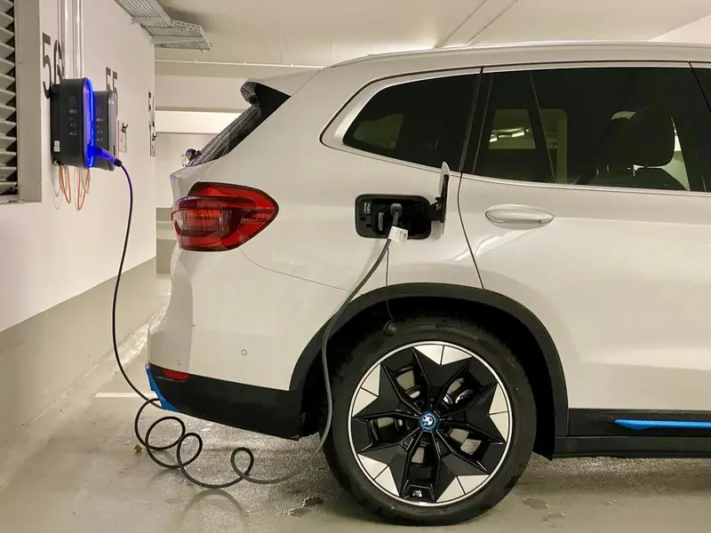 Coche eléctrico cargando en una plaza de garaje comunitario con el cargador en la pared